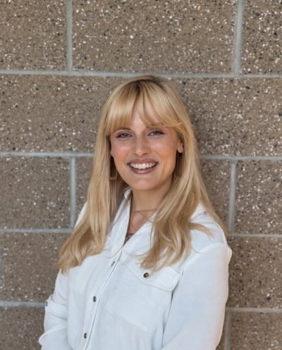 Smiling person with blonde hair in a white shirt against a brick wall, potentially involved in website design.